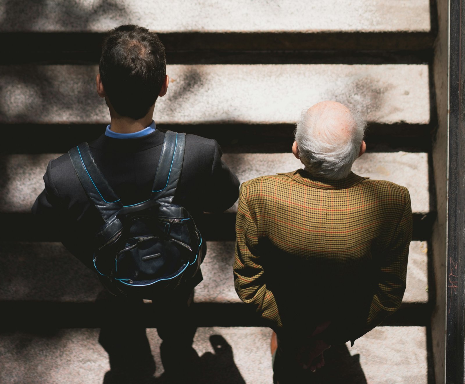 A younger person and an older person standing side by side on steps, seen from behind